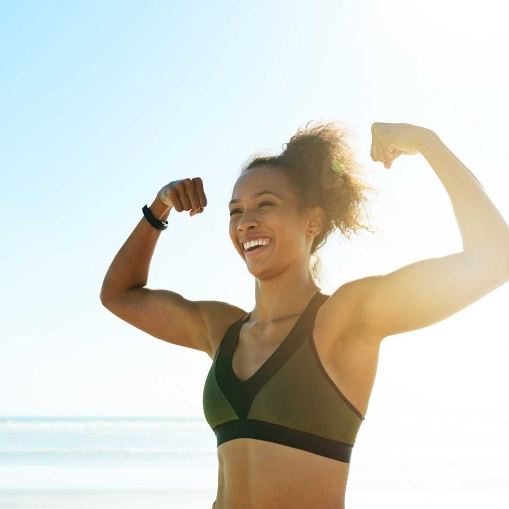 a woman flexing her biceps on a beach